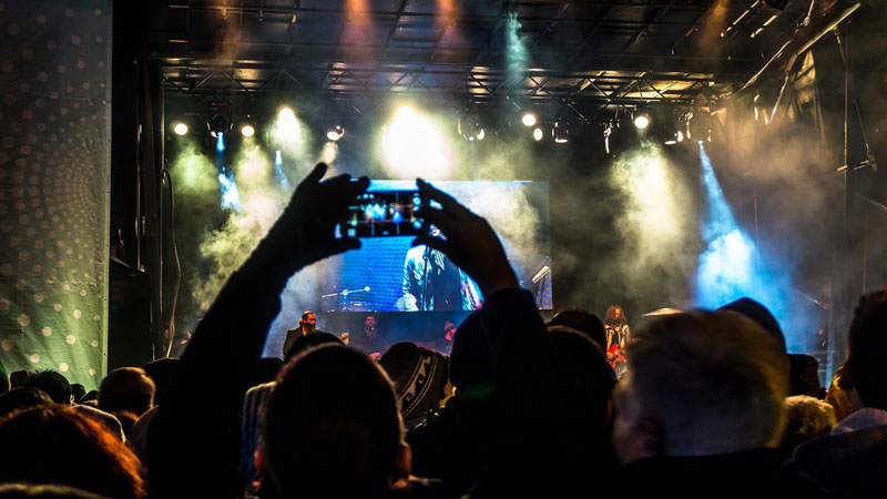 A band performs live as an audience member photographs them. Photo by Pexels.