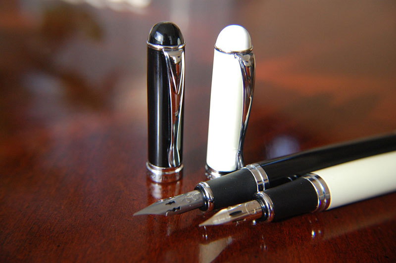 Two fountain pens on a dark brown desk, photo by Todabasura